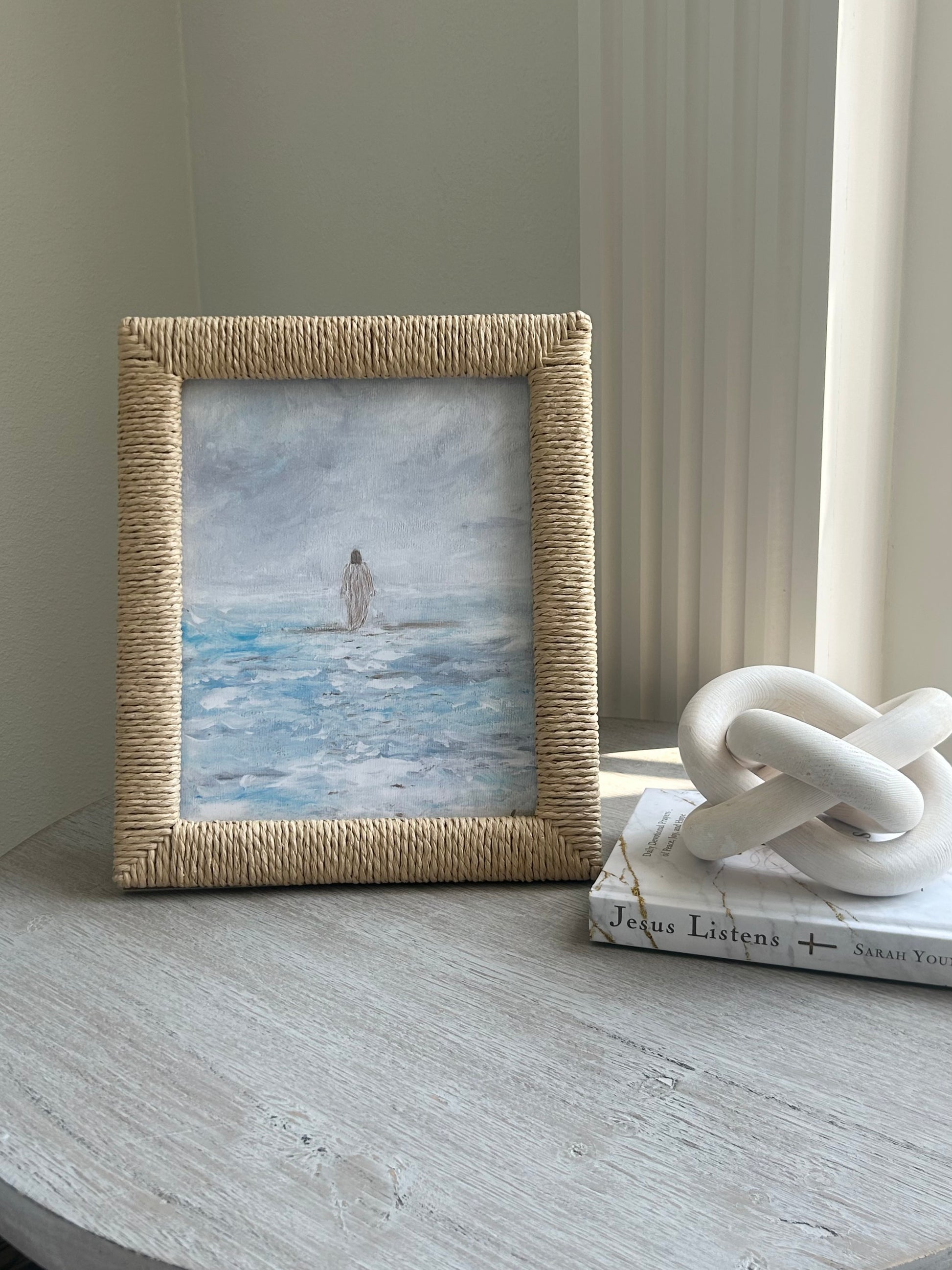 Framed artwork of a figure on water with a decorative knot sculpture and book in the background.